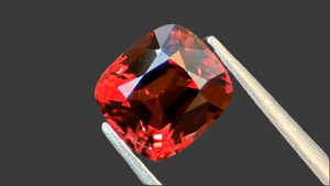 Vibrant orangey-red cushion-cut natural spinel gemstone, ethically sourced from Mogok, highlighted against a deep grey background, ideal for luxury fine jewellery.