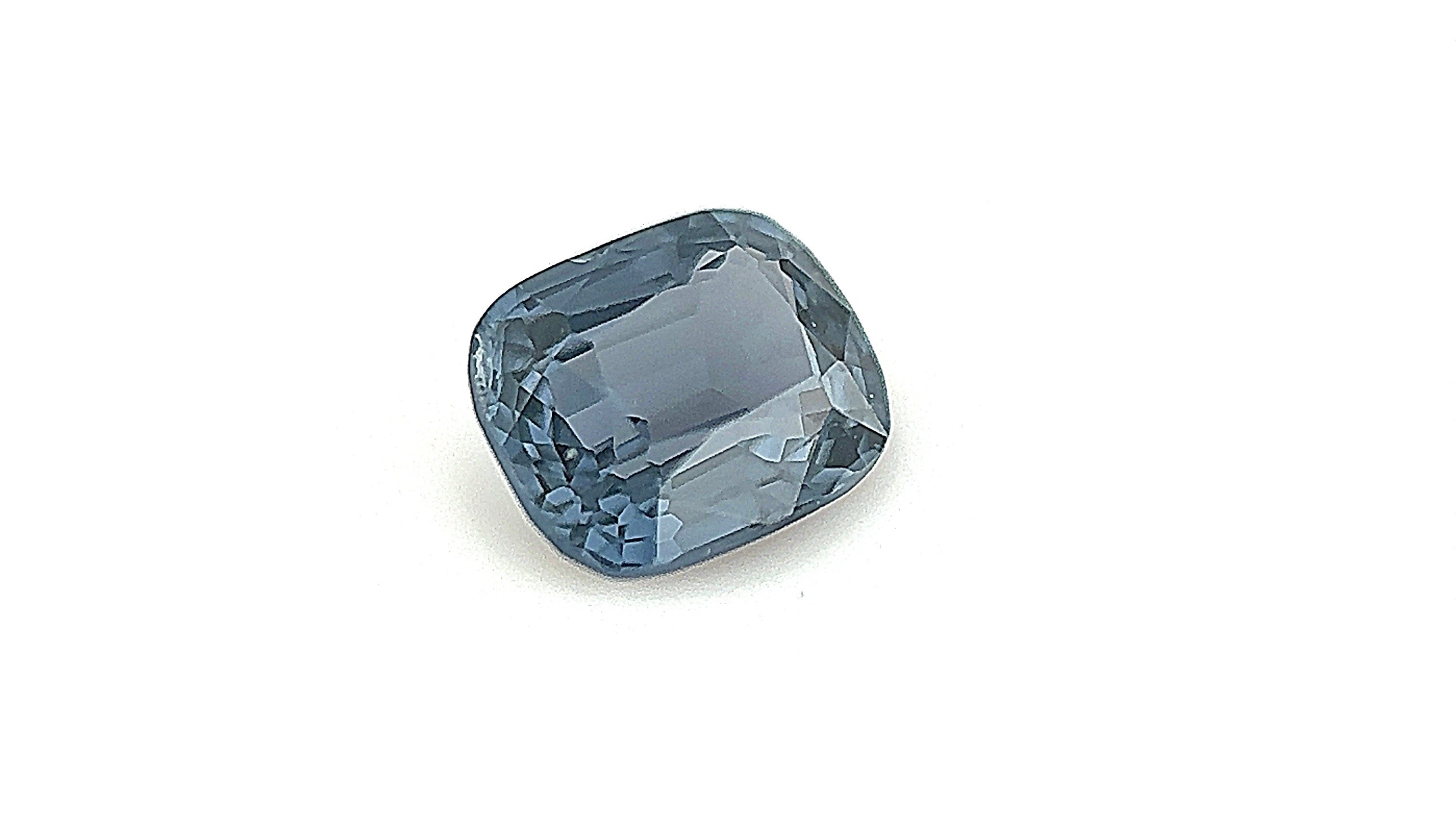 Close-up of a 0.85 carat greenish-blue natural spinel gemstone, displayed in a gemlight box, emphasizing its natural beauty.